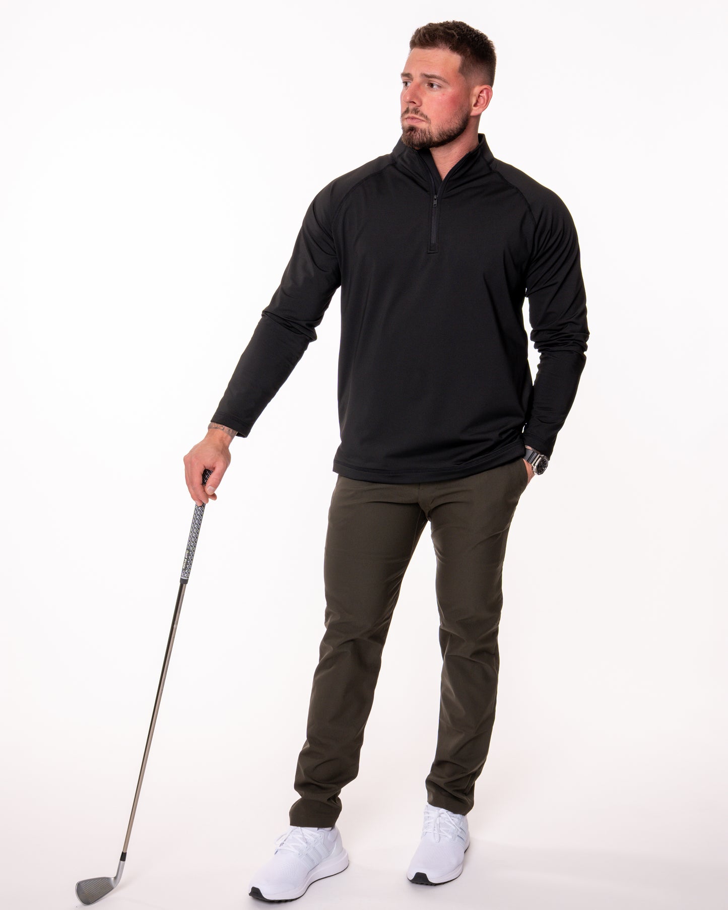 Man wearing a black quarter zip shirt holding a golf club